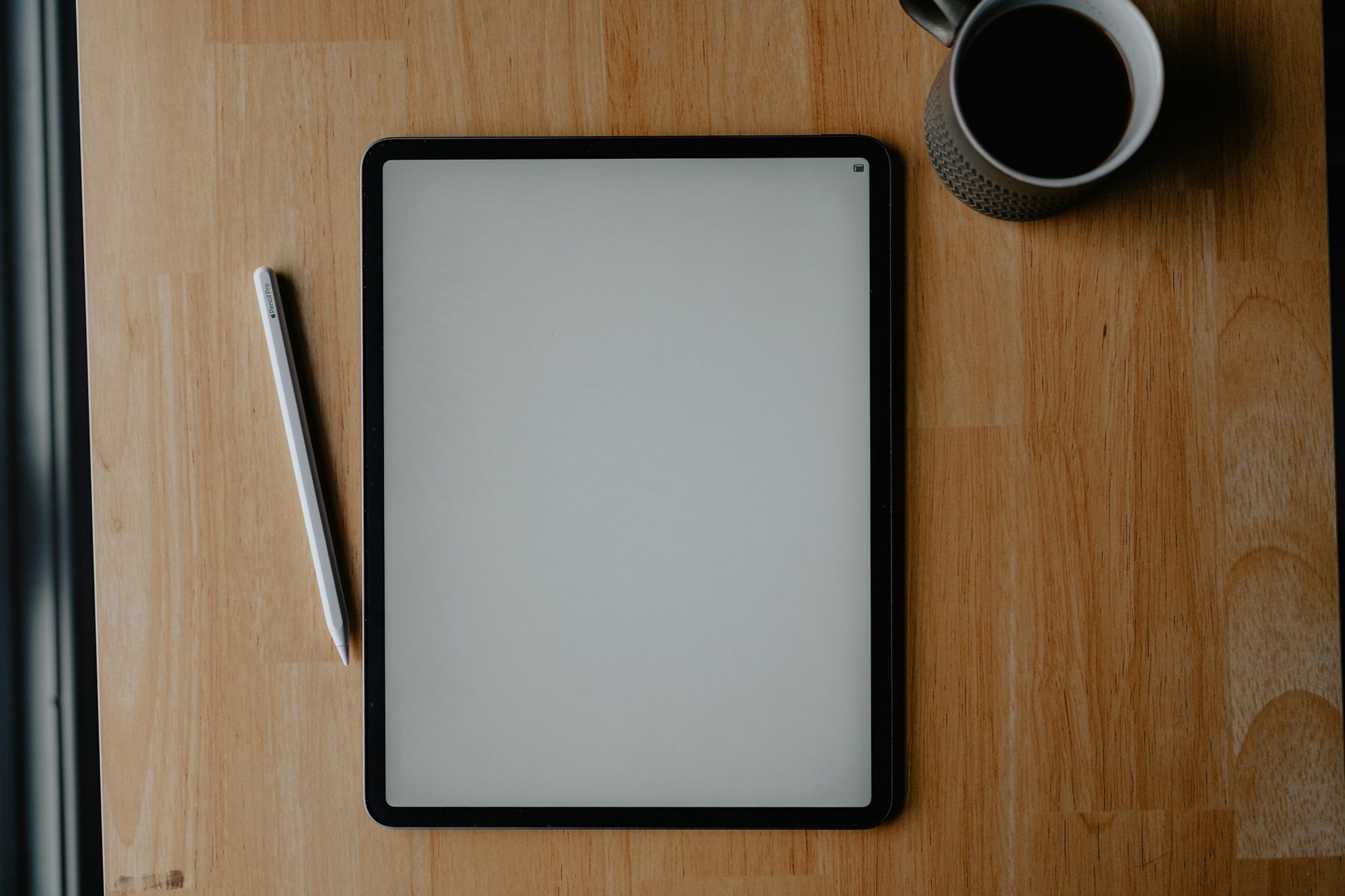 Tableta con la pantalla en blanco, un lápiz digital y una taza de café sobre una mesa de madera